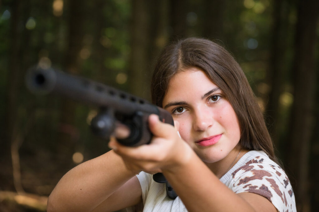 Outdoor senior photo of Bella with hunting gear highlighting her adventurous personality in Northern New York.